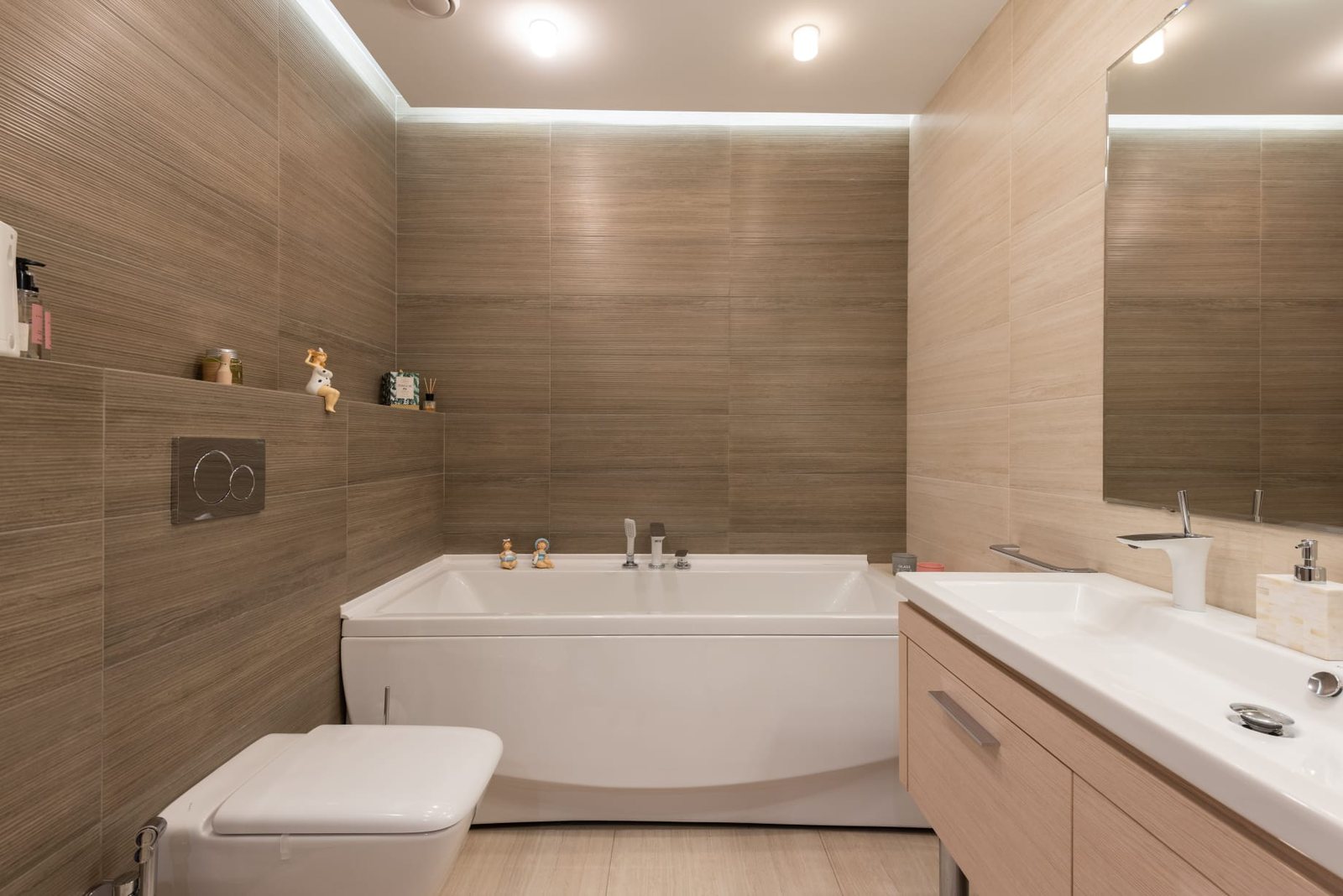 Ausgeführtes Badezimmer in warmer Holzoptik mit umlaufender Lichtvoute und eingebauter Badewanne