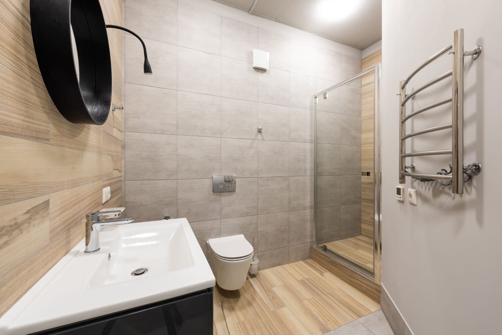 Ausgeführtes Badezimmer in Betonoptik mit hellem Holzboden und Dusche mit Klarglastür